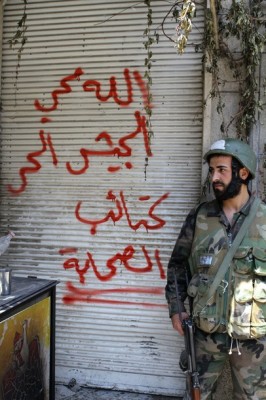 A Syrian soldier stands next to graffitis.jpeg