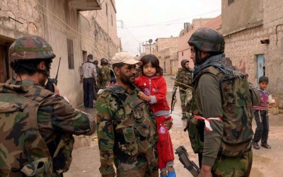A Syrian army soldier carries a child as they patrol the Sheik Said neighbourhood of Aleppo.jpg